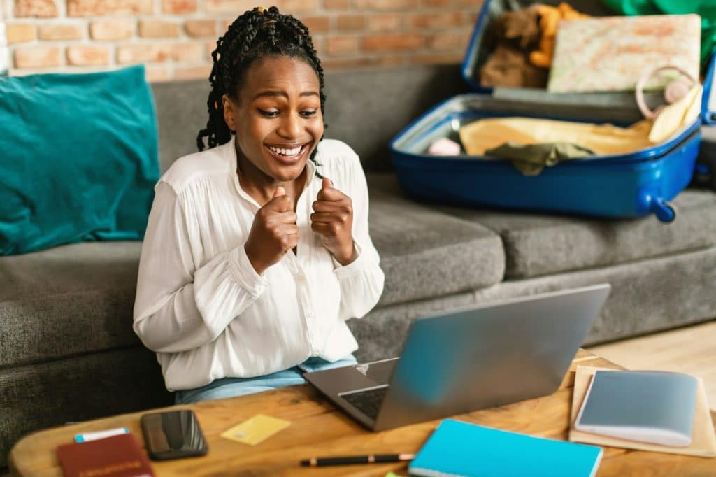 Hot tour, special travel offer. Happy black woman booking trip online via laptop, getting discount